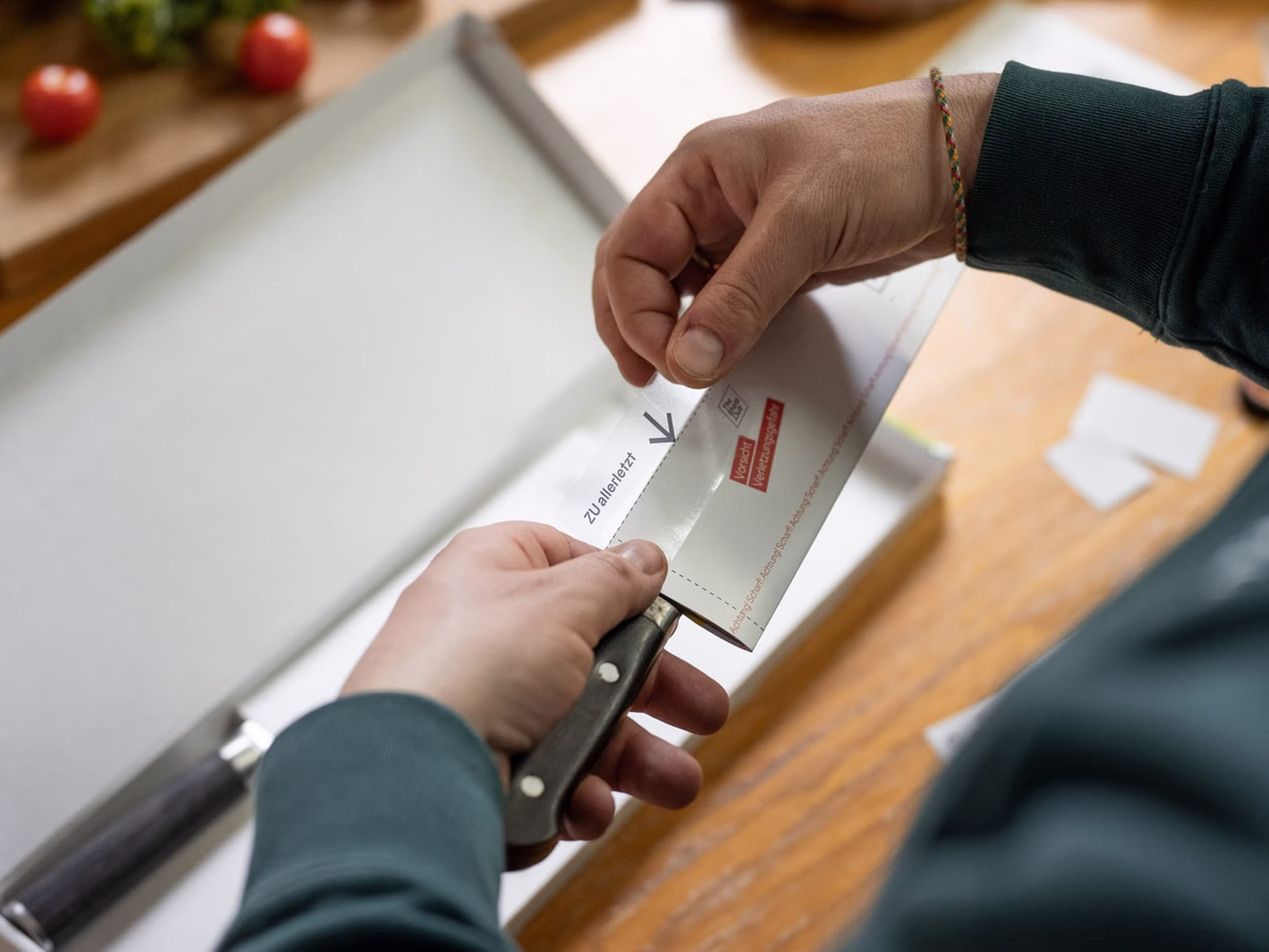 A hand slits open the TheSharp.Club packaging with a kitchen knife along the banderole.