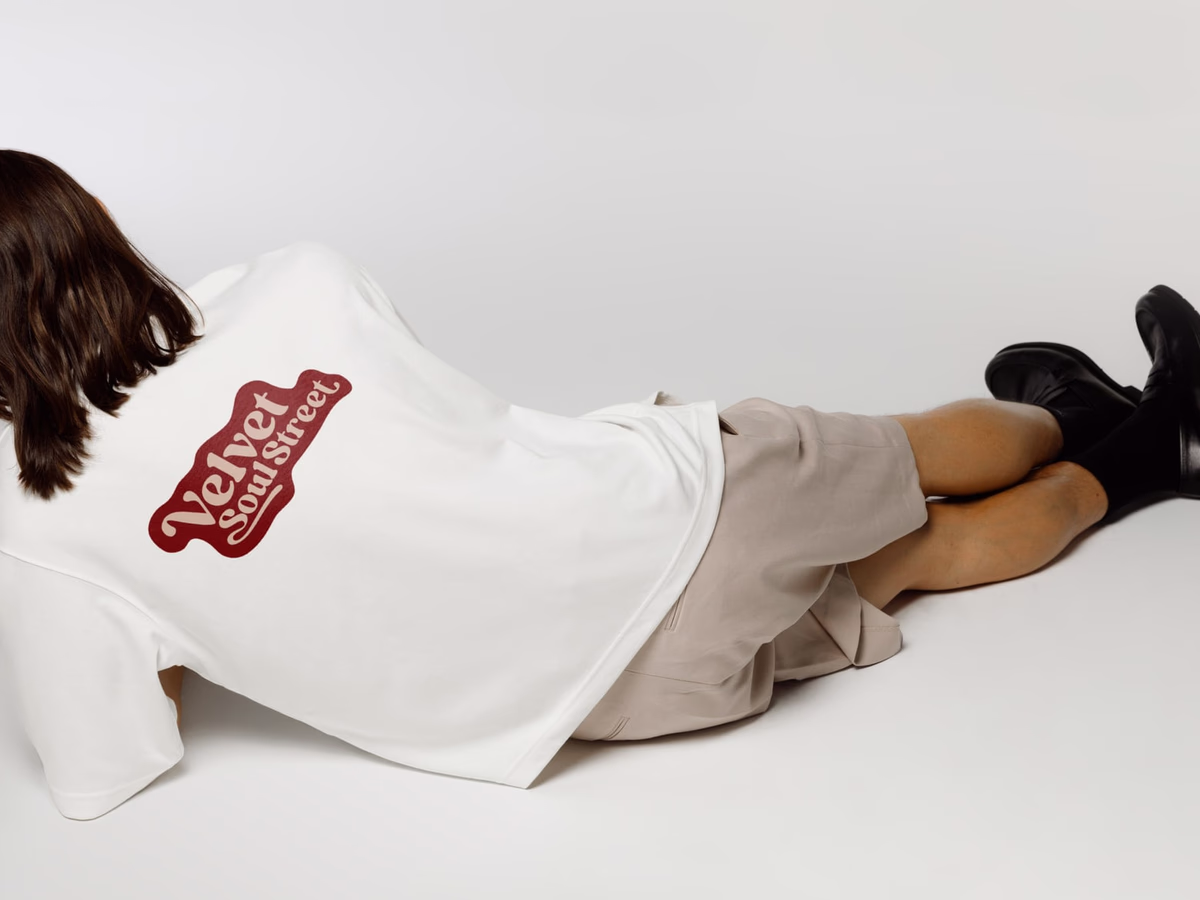 Person lies face-down on the floor, the red Velvet Soul Street logo printed across the back of a white shirt.