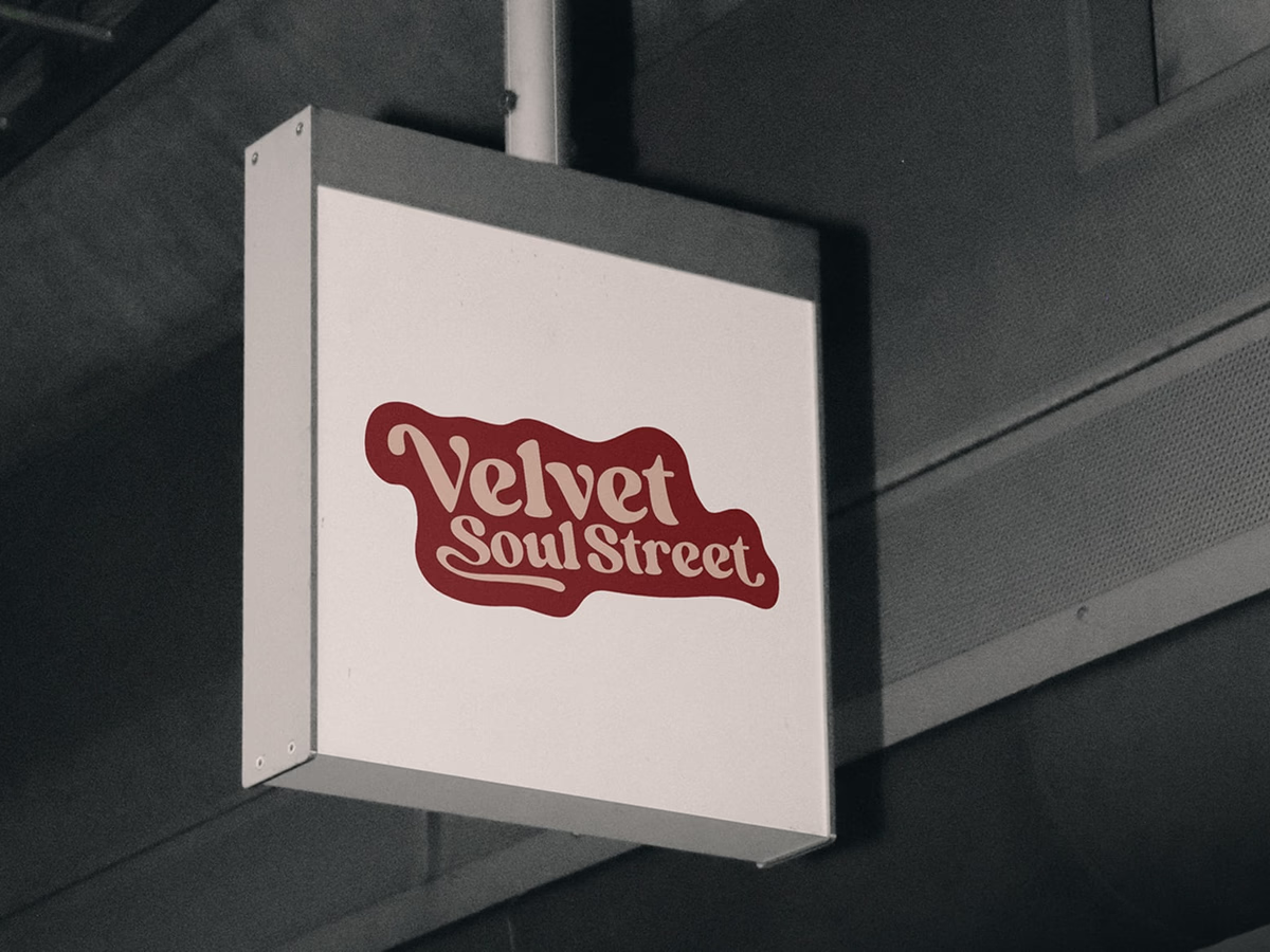 Illuminated shop sign with the Velvet Soul Street logo, hanging in a dark side street.