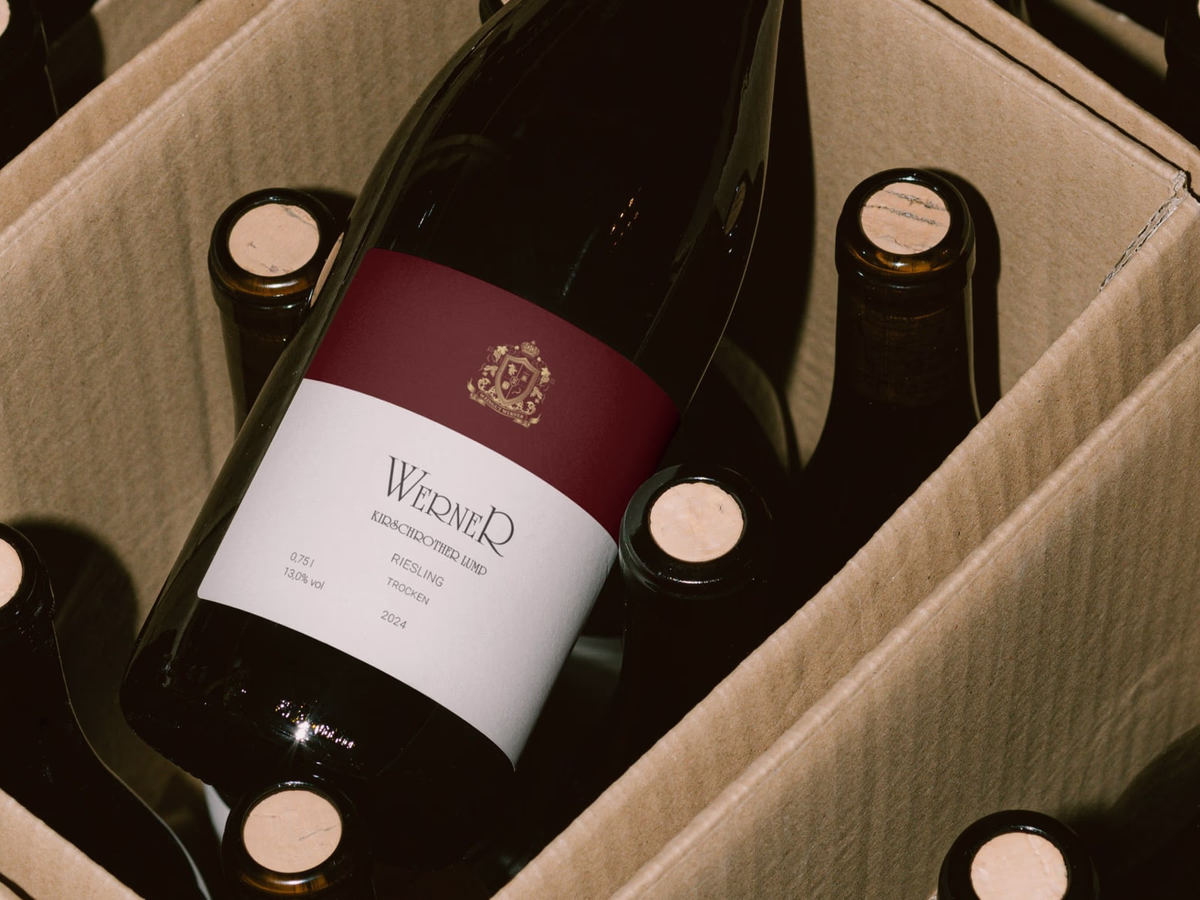 Red wine bottle with the Werner label resting in an opened corrugated six-pack carton.