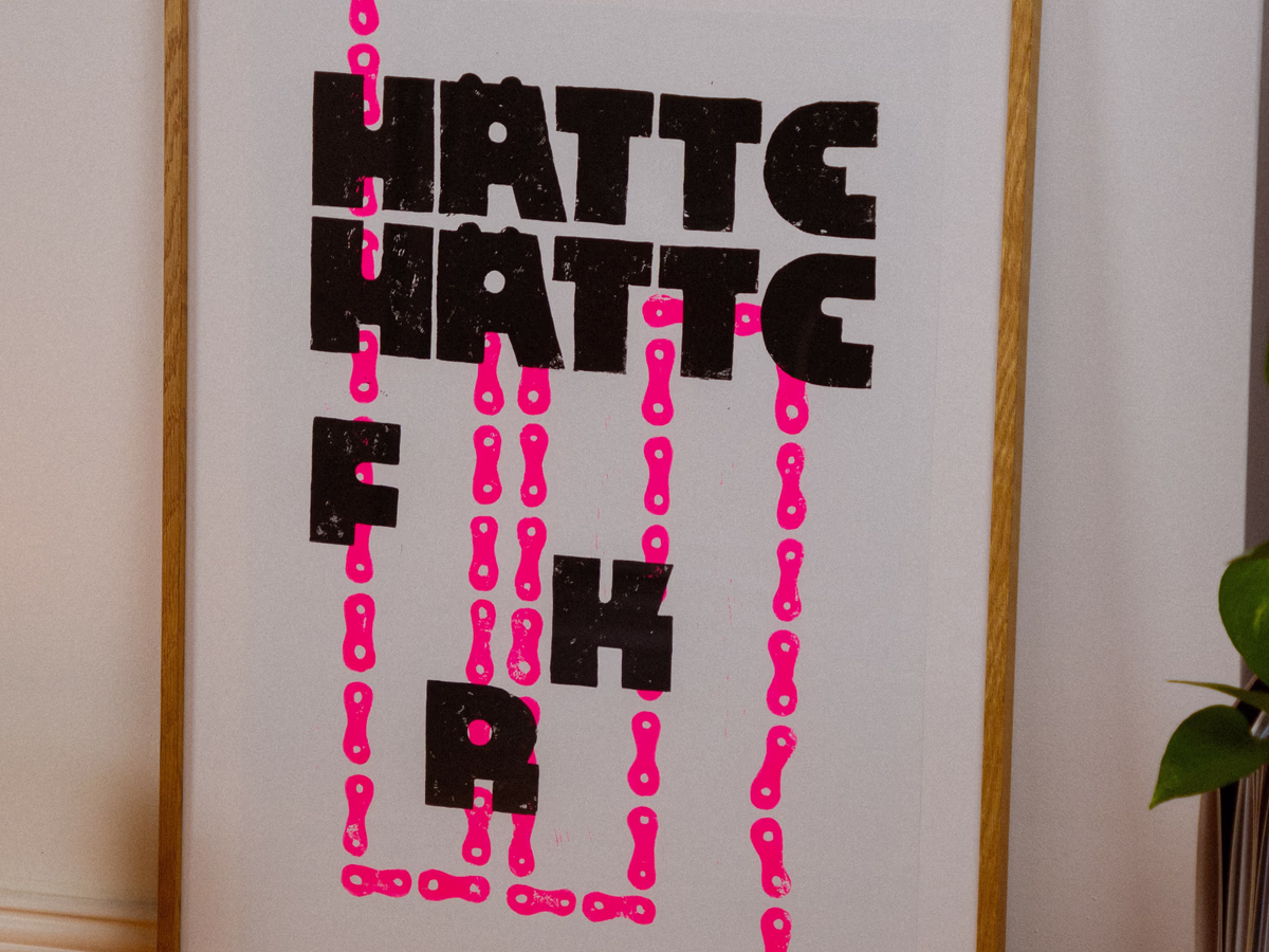 A2 poster "HÄTTE HÄTTE FAHRRADKETTE" in red linocut typography, leaning against a light wall.