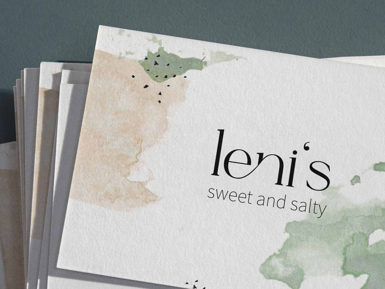 Stack of handmade watercolour menu cards with the leni's sweet and salty wordmark on a light surface.