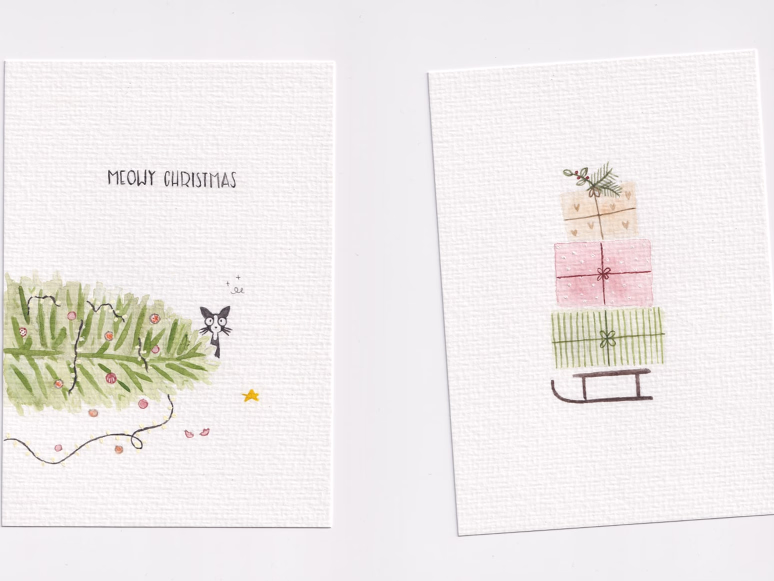 Two hand-drawn Christmas postcards side by side — a sleigh with gifts and a Christmas tree with a cat.